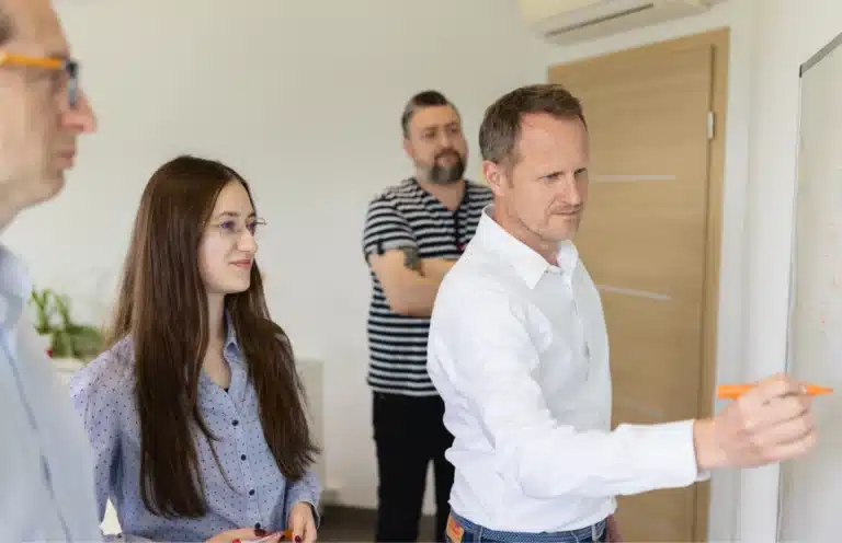 Équipe XS Groupe réunie autour d'un collaborateur qui écrit sur un tableau blanc